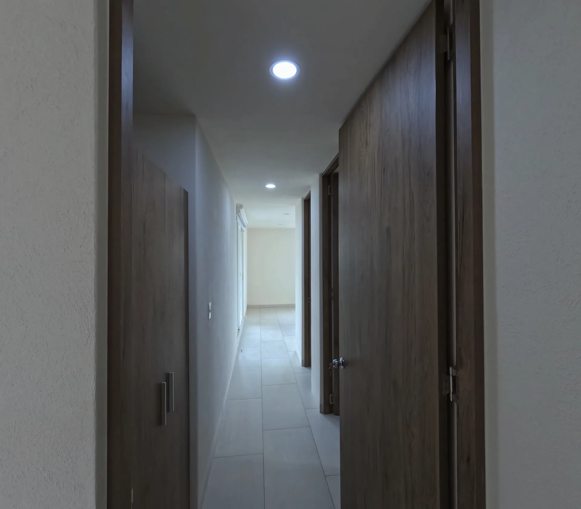 Pasillo interior de distribucion con puertas de madera y piso de loseta gris.