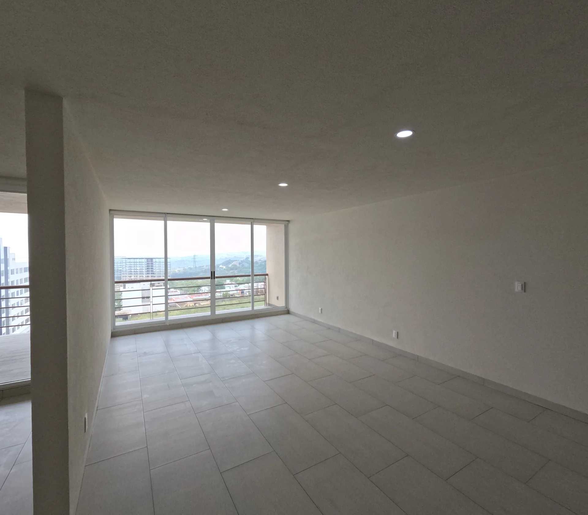 Sala de departamento con balcon corrido, piso de loseta gris y vista hacia el entorno.