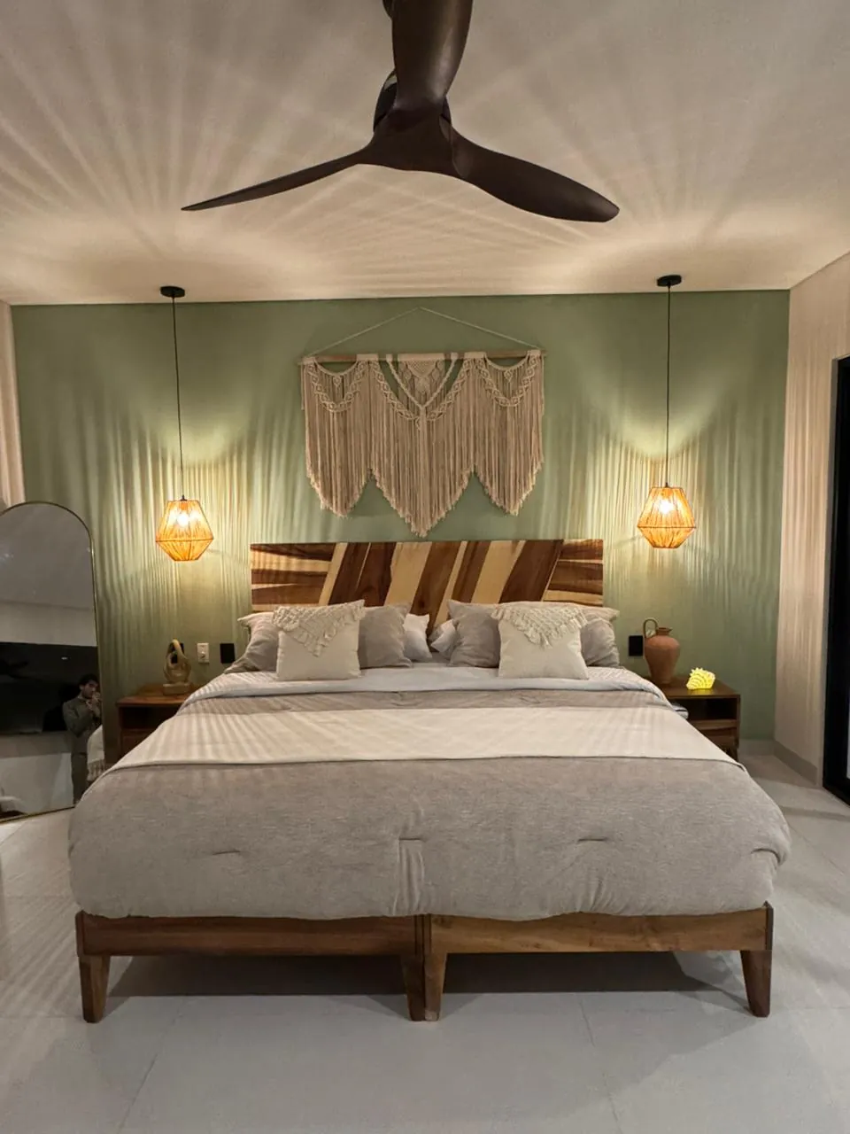 Recámara principal tipo: cama king, cabecero de madera con manta decorativa, ventilador de techo y mesitas de noche con jarra de barro.